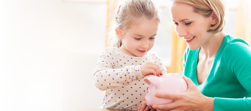 Mother is watching young daughter put coins in piggy bank.