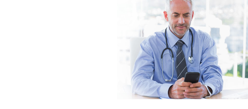 Man with stethoscope around his neck is sitting down looking at his cell phone.